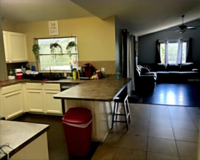 kitchen with dark tile patterned floors, ceiling fan, a breakfast bar area, and white cabinets