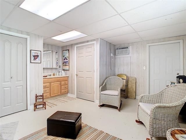 sitting room with a paneled ceiling, wooden walls, concrete floors, and a wall mounted air conditioner