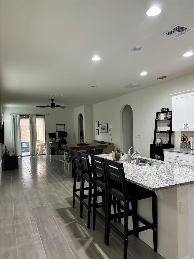 kitchen with light stone countertops, white cabinets, a center island with sink, and a kitchen bar