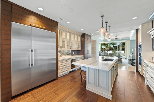 kitchen featuring appliances with stainless steel finishes, an island with sink, pendant lighting, hardwood / wood-style floors, and sink