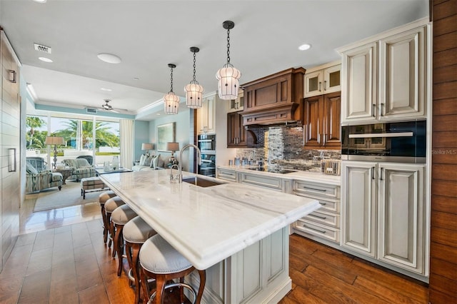 kitchen with dark hardwood / wood-style floors, tasteful backsplash, sink, an island with sink, and light stone countertops