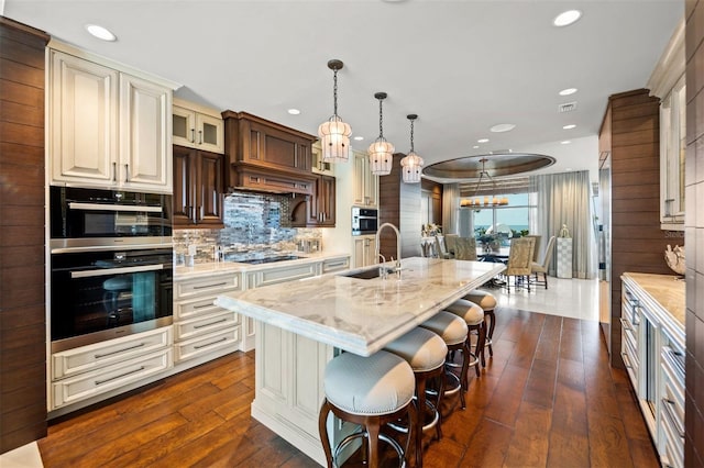 kitchen featuring an island with sink, decorative light fixtures, sink, and dark hardwood / wood-style flooring