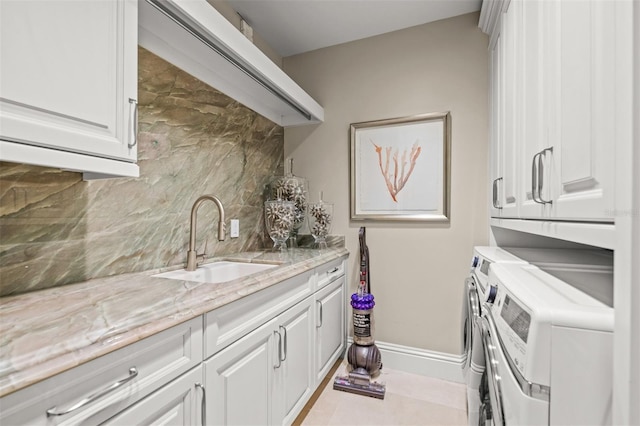 clothes washing area featuring light tile patterned floors, a sink, baseboards, washer and dryer, and cabinet space