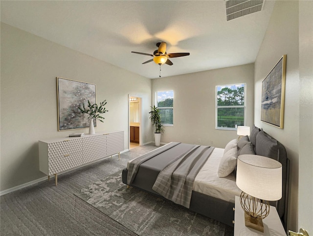 bedroom featuring ceiling fan, ensuite bathroom, and dark carpet