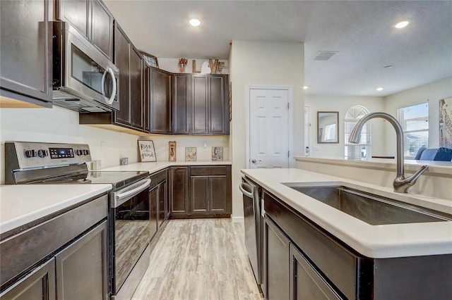 kitchen featuring dark brown cabinetry, appliances with stainless steel finishes, sink, and light hardwood / wood-style flooring