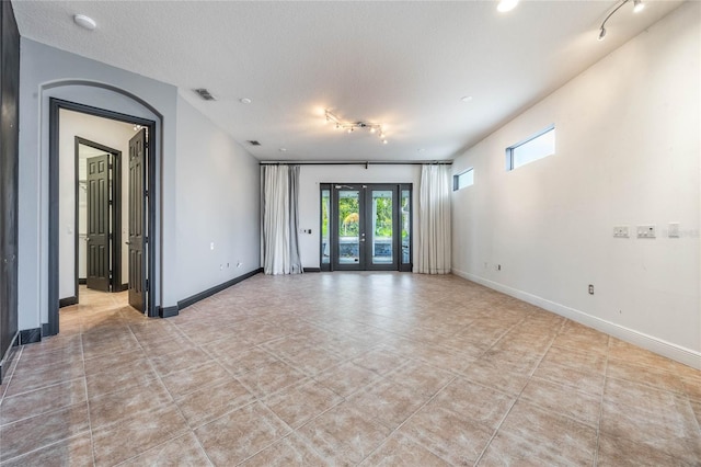 tiled spare room featuring french doors, track lighting, and a textured ceiling