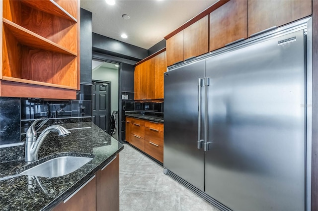 kitchen with built in refrigerator, sink, decorative backsplash, and dark stone counters