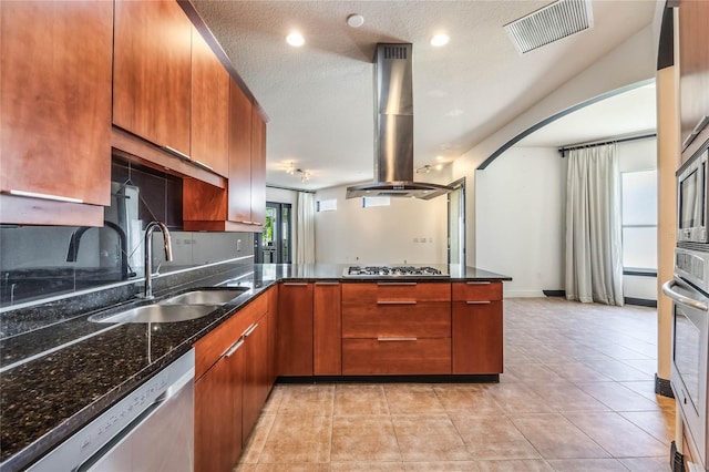 kitchen with island exhaust hood, stainless steel appliances, dark stone counters, sink, and a textured ceiling