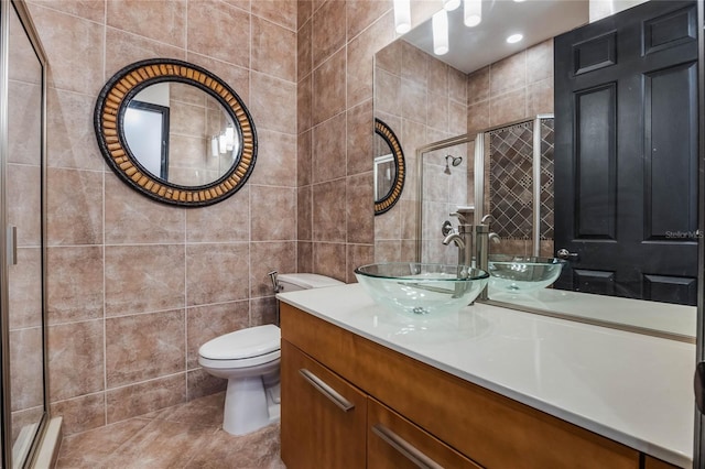 bathroom with a shower with door, toilet, tile patterned floors, tile walls, and vanity