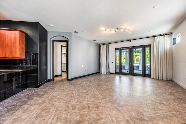 unfurnished room with a textured ceiling, light tile patterned floors, visible vents, baseboards, and french doors