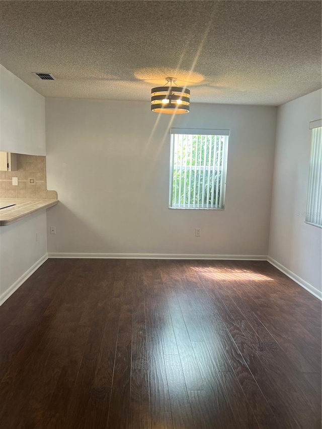 spare room with dark wood-type flooring, a textured ceiling, and an inviting chandelier