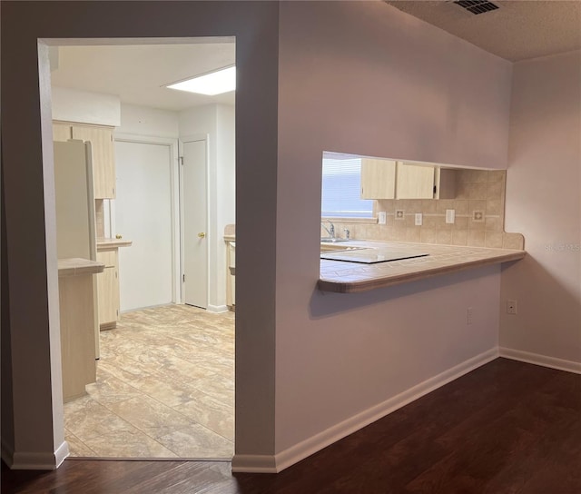 kitchen with decorative backsplash, cream cabinetry, white refrigerator, and light hardwood / wood-style floors