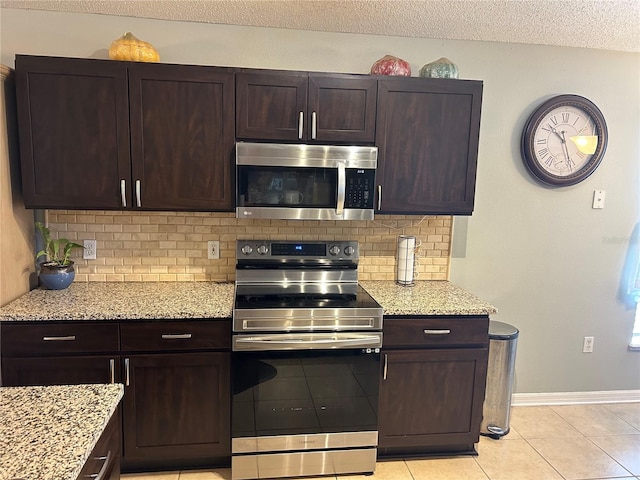 kitchen with light tile patterned flooring, light stone counters, backsplash, stainless steel appliances, and dark brown cabinetry