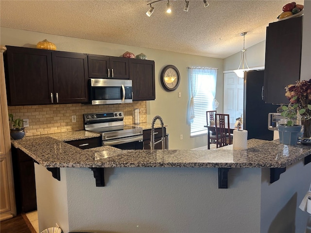 kitchen with appliances with stainless steel finishes, backsplash, vaulted ceiling, and a kitchen breakfast bar