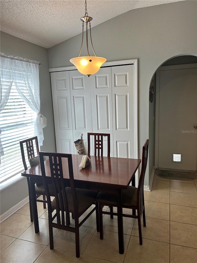 dining room with a textured ceiling, lofted ceiling, and light tile patterned floors