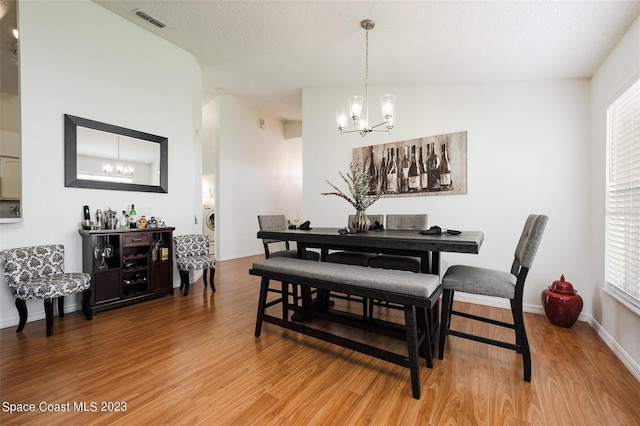 dining space with an inviting chandelier, vaulted ceiling, a textured ceiling, and hardwood / wood-style flooring