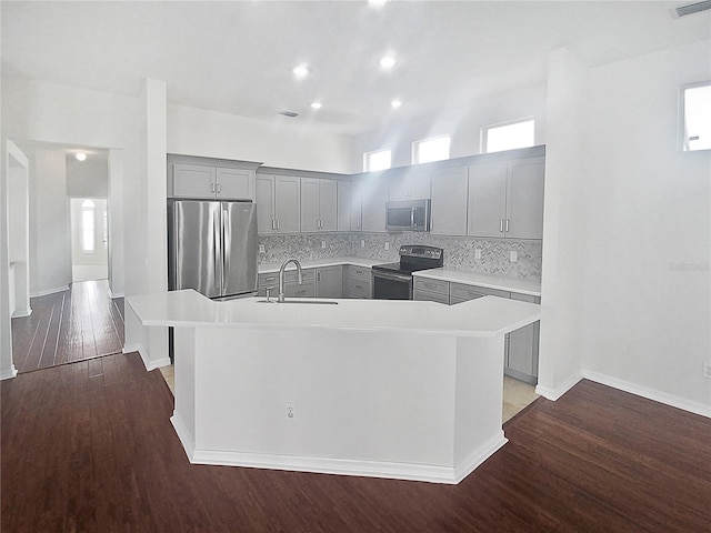 kitchen with tasteful backsplash, a kitchen island with sink, gray cabinets, stainless steel appliances, and dark hardwood / wood-style flooring