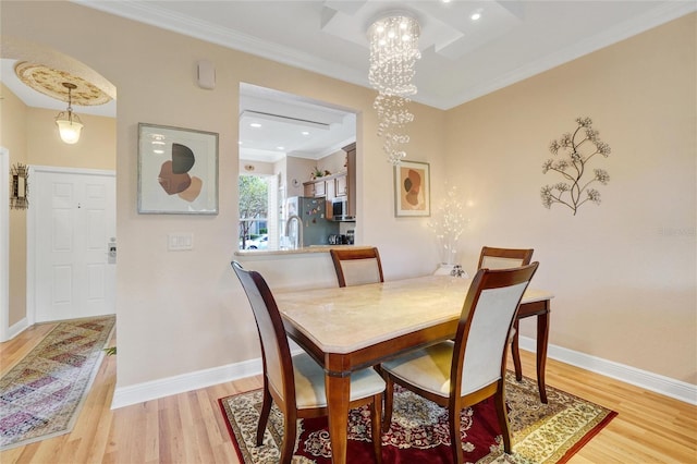 dining space with crown molding, light hardwood / wood-style floors, and a notable chandelier