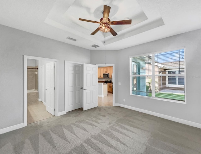 unfurnished bedroom with a raised ceiling, ceiling fan, light colored carpet, and ensuite bathroom