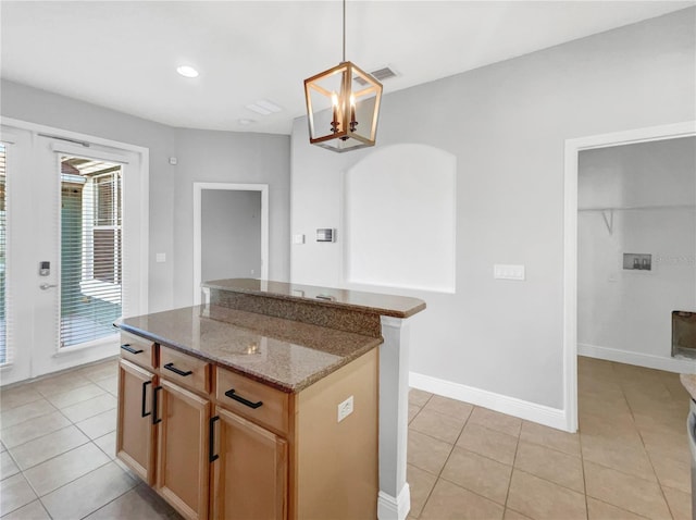 kitchen with pendant lighting, a kitchen island, light tile patterned floors, and dark stone counters