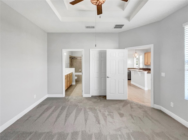 unfurnished bedroom with a raised ceiling, ensuite bath, ceiling fan, and light colored carpet