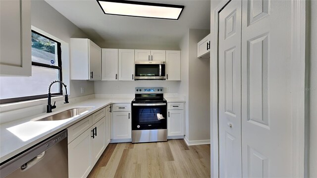 kitchen featuring appliances with stainless steel finishes, light wood-type flooring, sink, and white cabinets