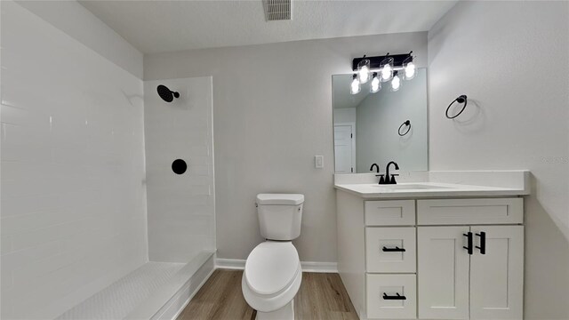 bathroom with hardwood / wood-style floors, tiled shower, vanity, and toilet