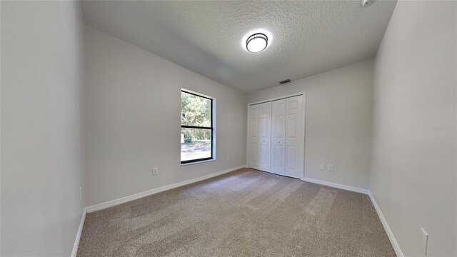 unfurnished bedroom with a closet, lofted ceiling, a textured ceiling, and carpet floors