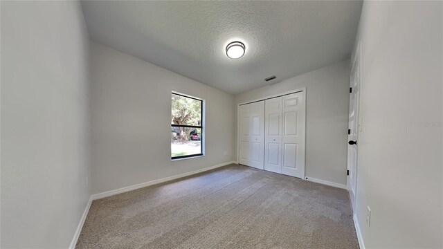 unfurnished bedroom featuring a textured ceiling, carpet, lofted ceiling, and a closet