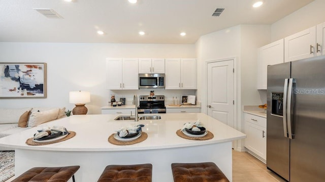 kitchen featuring a breakfast bar area, a center island with sink, stainless steel appliances, and white cabinetry