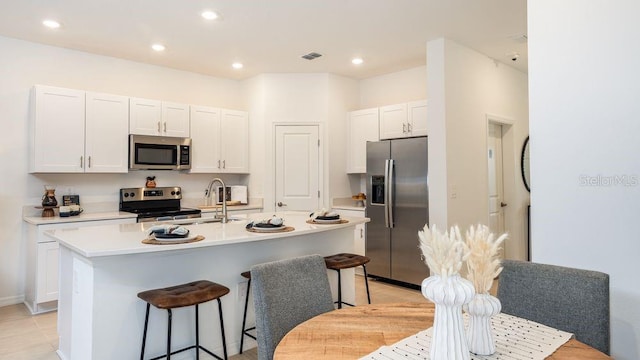 kitchen with a breakfast bar, a kitchen island with sink, sink, white cabinets, and stainless steel appliances