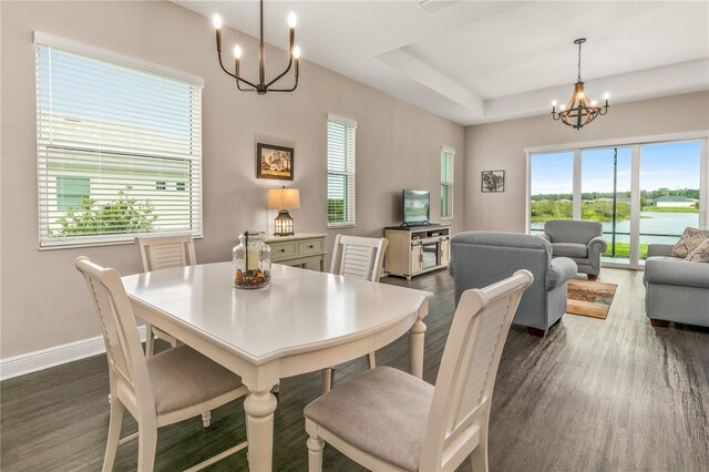 dining space with an inviting chandelier, dark wood-type flooring, a raised ceiling, and baseboards