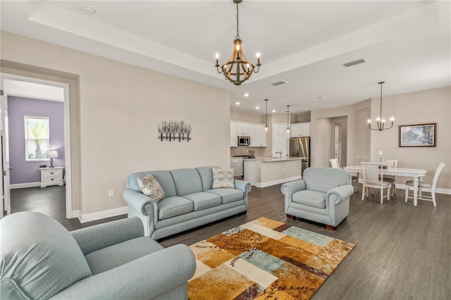 living room with a chandelier, a raised ceiling, dark wood-type flooring, visible vents, and baseboards