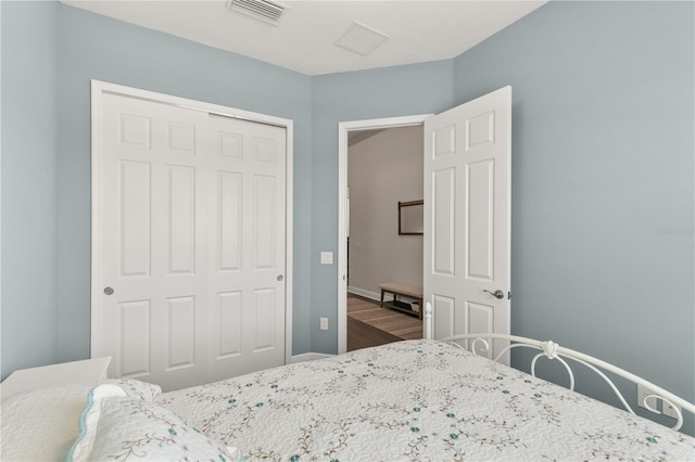 bedroom featuring wood finished floors, visible vents, baseboards, and a closet