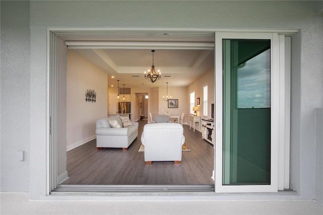 living room with a tray ceiling, an inviting chandelier, and dark wood-type flooring