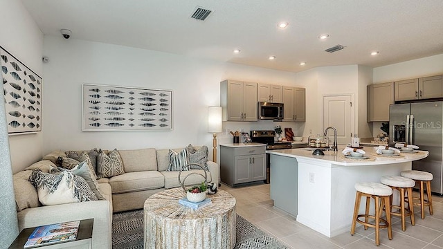 kitchen with gray cabinets, a kitchen island with sink, light tile patterned floors, and stainless steel appliances