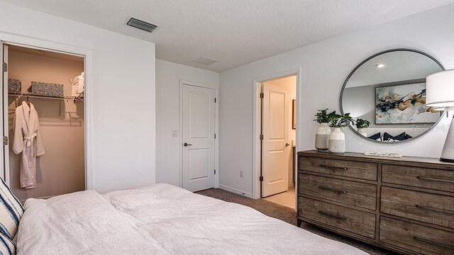 carpeted bedroom featuring a closet, a walk in closet, and a textured ceiling