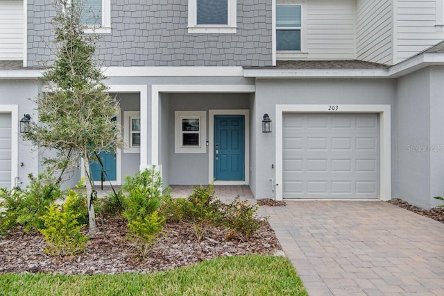 entrance to property with stucco siding, an attached garage, and decorative driveway