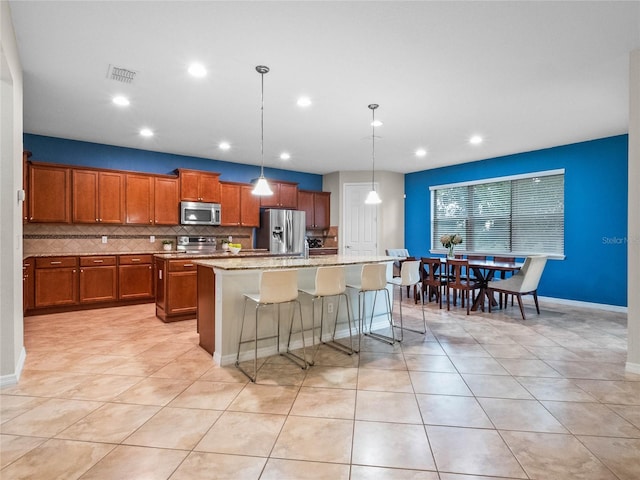 kitchen with a breakfast bar, tasteful backsplash, decorative light fixtures, appliances with stainless steel finishes, and a kitchen island with sink