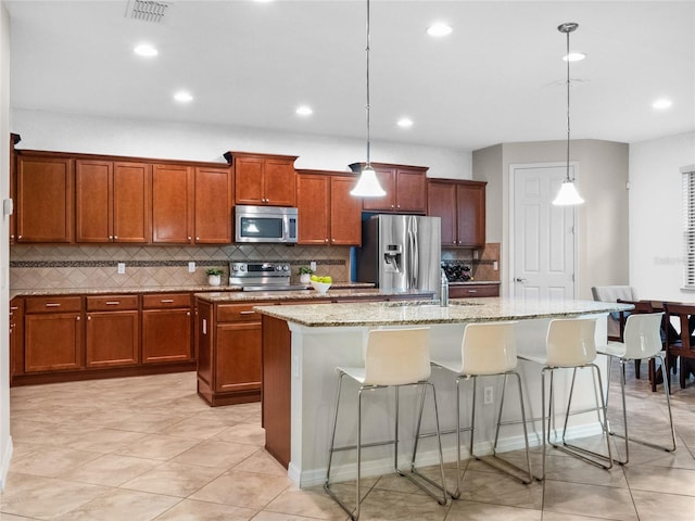 kitchen featuring a kitchen island with sink, stainless steel appliances, light stone counters, a kitchen bar, and decorative light fixtures