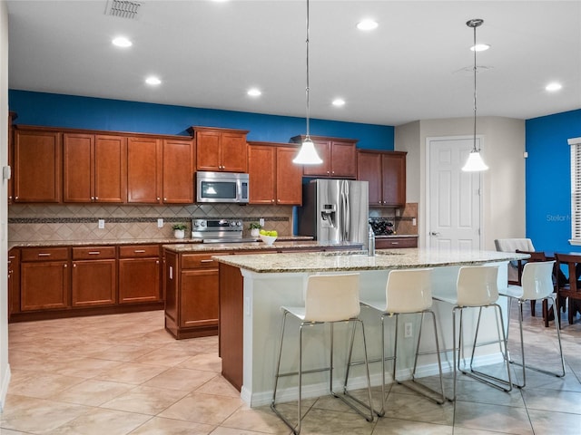 kitchen featuring stainless steel appliances, a kitchen island with sink, pendant lighting, and a kitchen bar