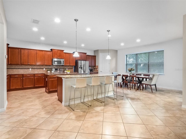 kitchen featuring decorative light fixtures, a center island with sink, appliances with stainless steel finishes, a kitchen breakfast bar, and backsplash