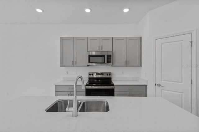 kitchen with gray cabinetry, light countertops, recessed lighting, appliances with stainless steel finishes, and a sink