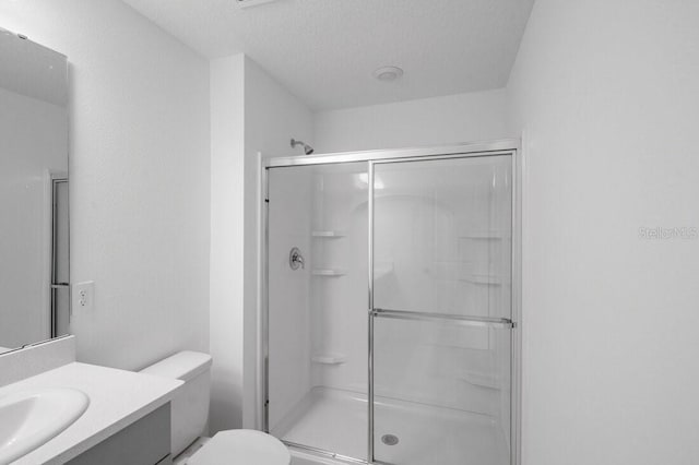 full bath with toilet, a stall shower, vanity, and a textured ceiling