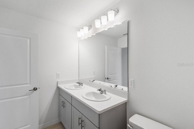 bathroom featuring double vanity, a textured ceiling, toilet, and a sink