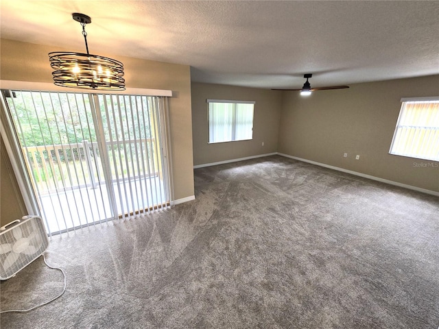 carpeted empty room featuring a textured ceiling and ceiling fan with notable chandelier