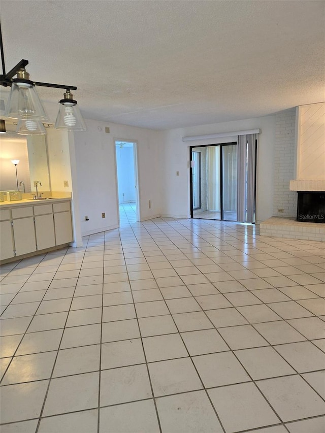 unfurnished living room featuring a fireplace, light tile patterned floors, a textured ceiling, and sink