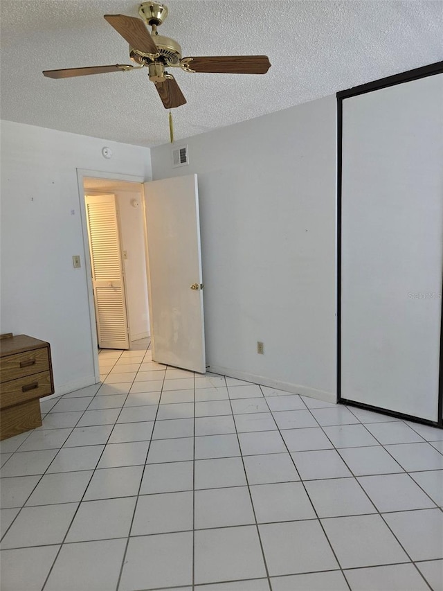 unfurnished bedroom with light tile patterned floors, a textured ceiling, a closet, and ceiling fan