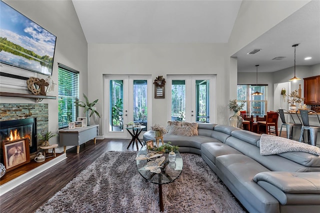 living room with vaulted ceiling, a stone fireplace, french doors, and dark hardwood / wood-style flooring