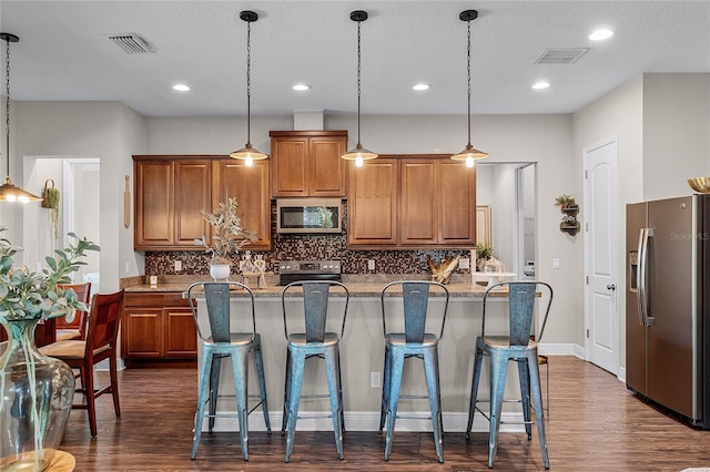 kitchen featuring decorative light fixtures, an island with sink, appliances with stainless steel finishes, and decorative backsplash